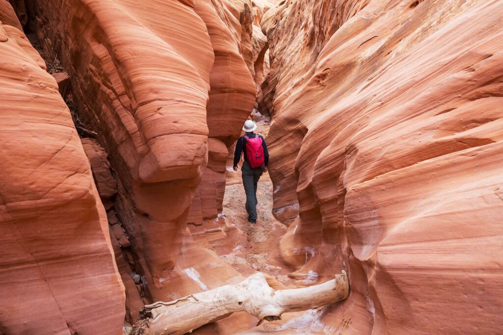 Hiker walking through a narrow red rock slot canyon in Escalante Utah