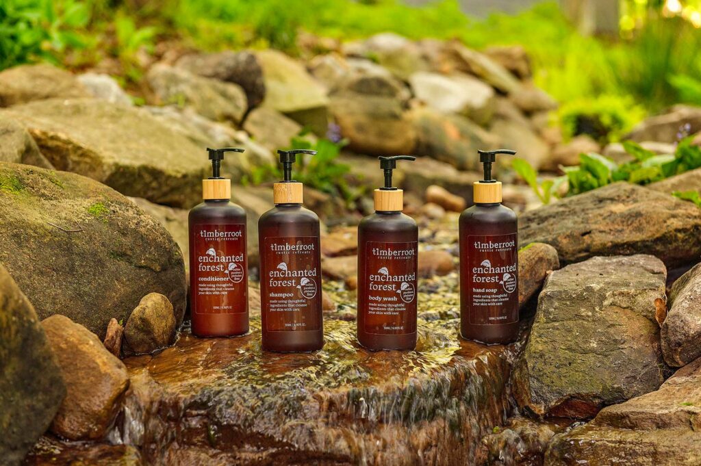 Timberroot Enchanted Forest shampoo, conditioner, body wash, and hand soap displayed beside a flowing creek