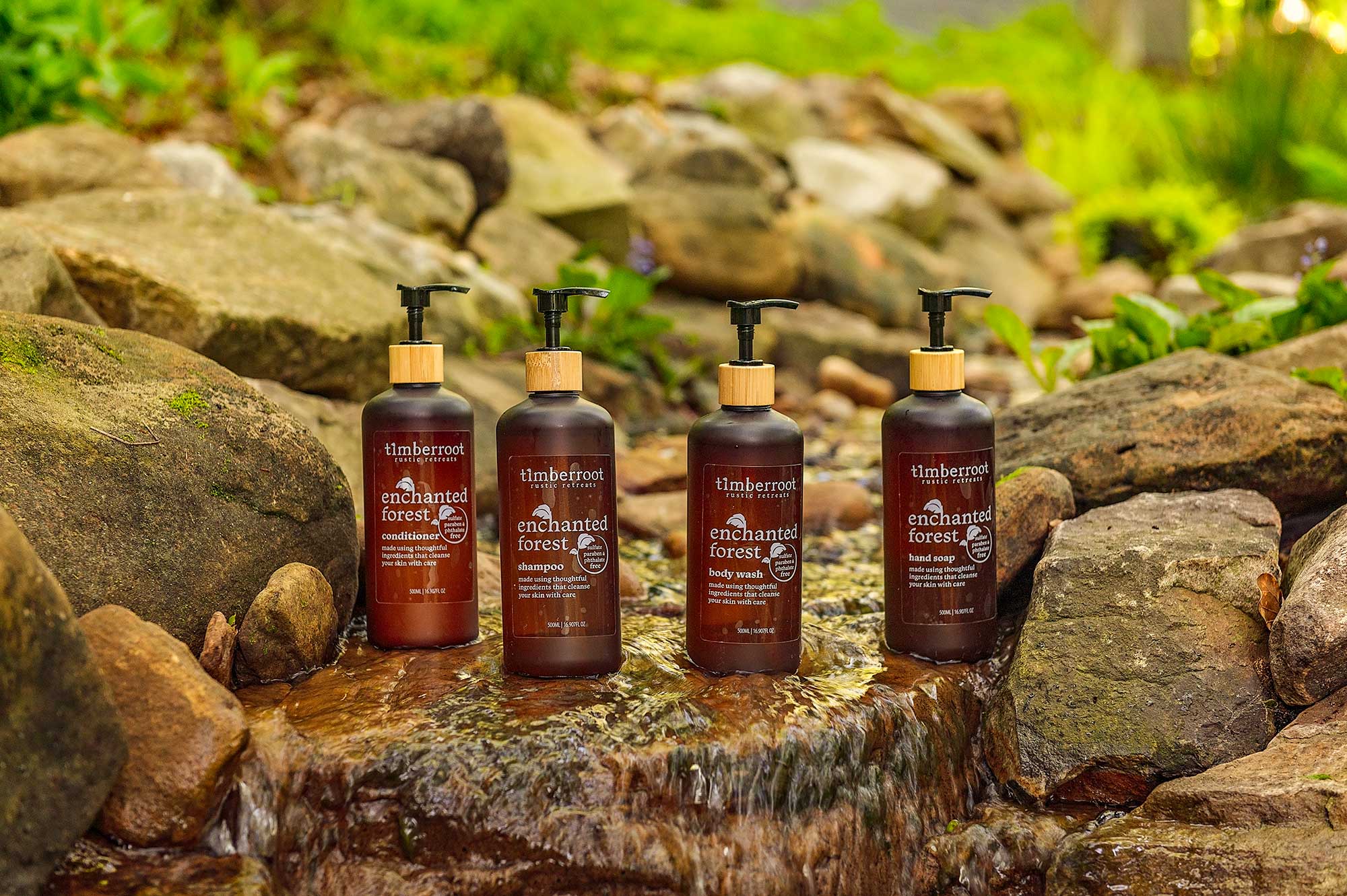 Timberroot Enchanted Forest shampoo, conditioner, body wash, and hand soap displayed beside a flowing creek